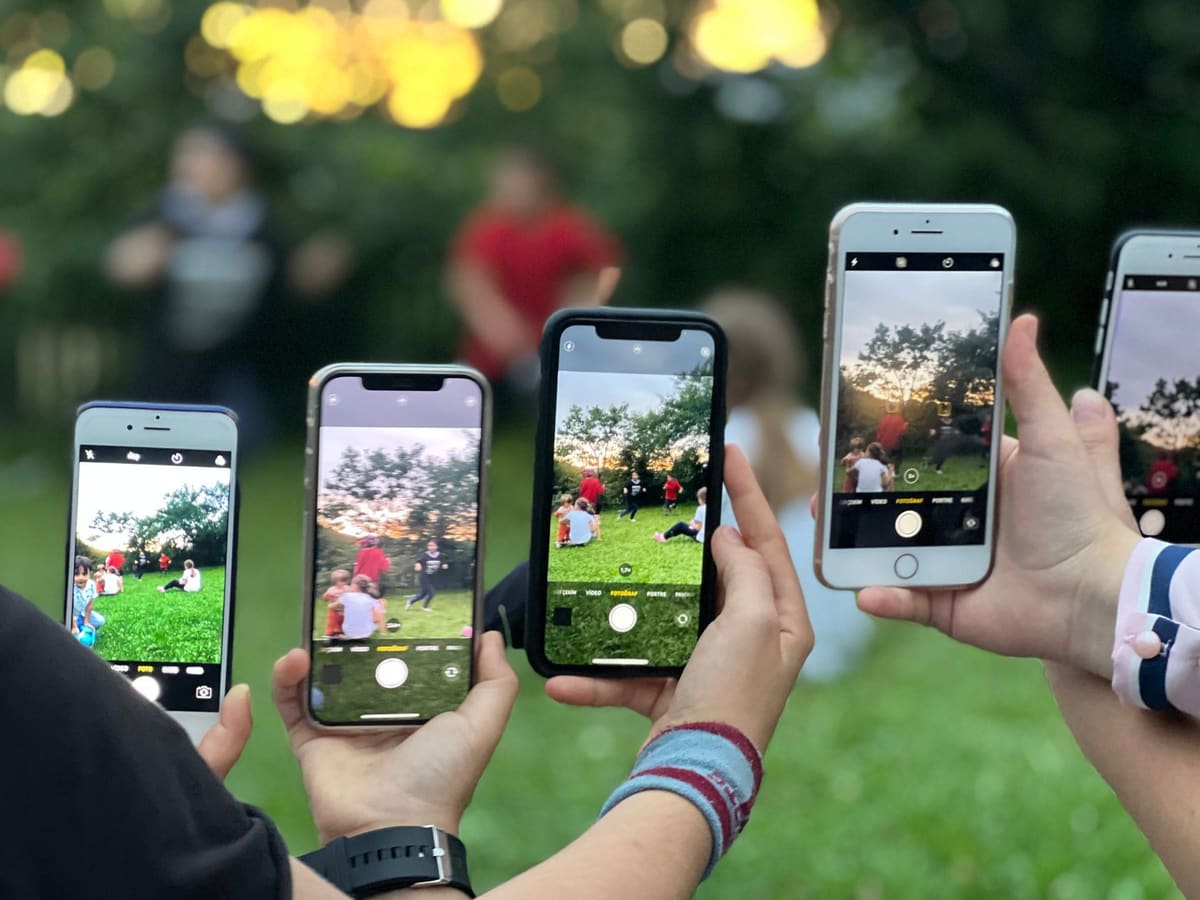 A crowd of friends all holding up their phones to photograph the same moment at dusk